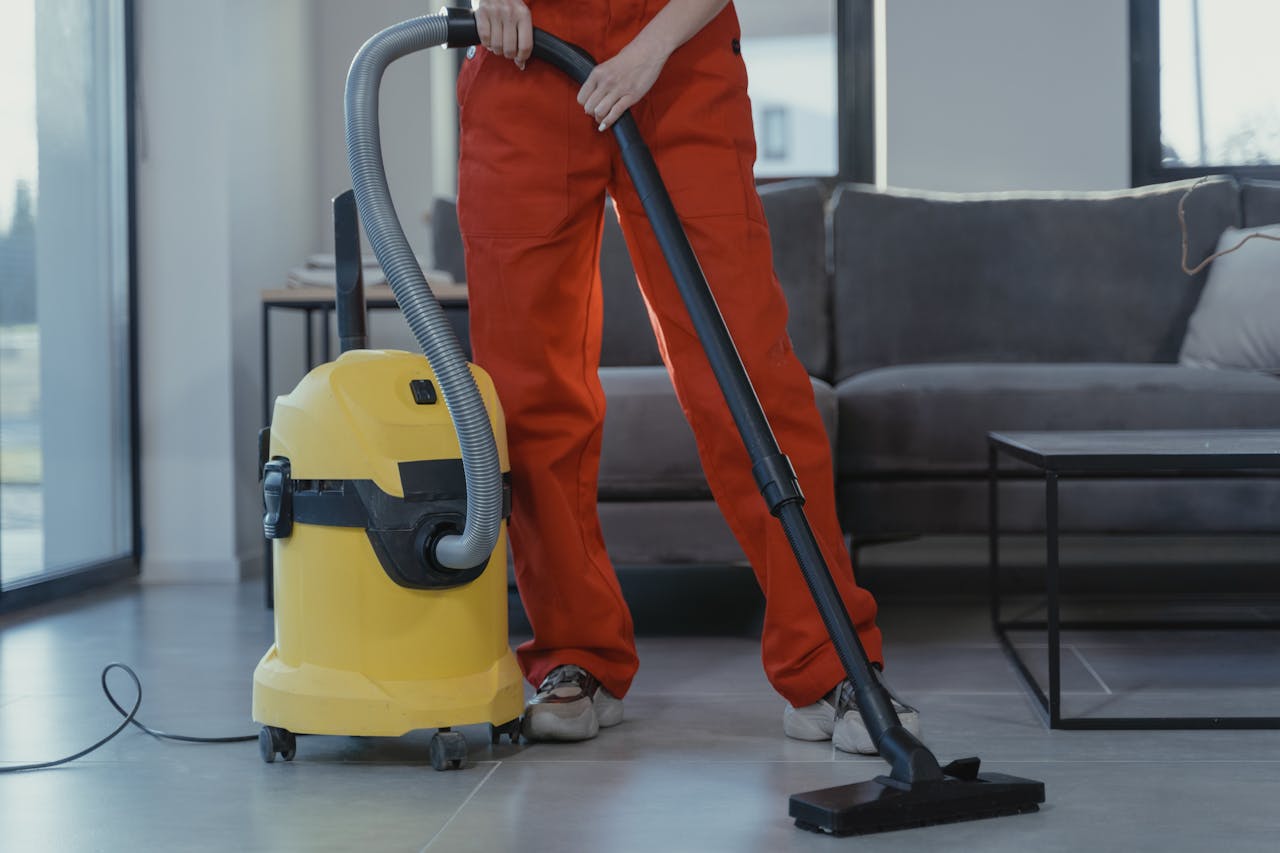 about-us A professional cleaner in red coveralls vacuums a contemporary living room with a yellow vacuum cleaner.